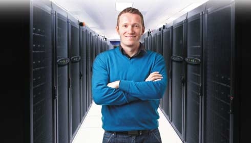 一位男士站在数据中心前方，手臂交叉，并对着相机微笑。