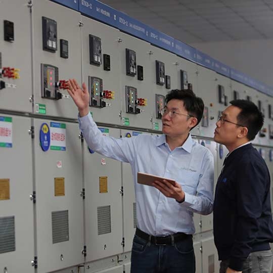 Two male employee discussing while standing besides control panels